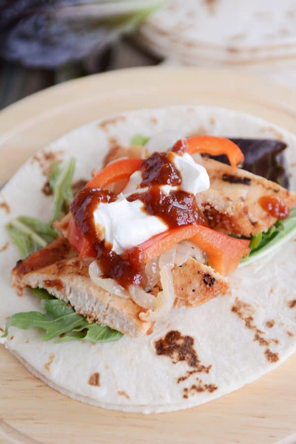 A grilled chipotle chicken wrap with sour cream, peppers, and salsa on top.