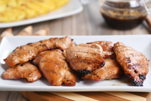 Grilled hawaiian chicken thighs on white platter.