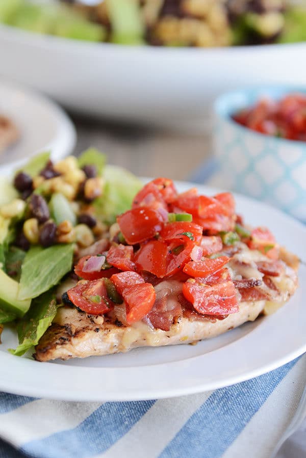 A grilled chicken breast topped with sliced tomatoes, and a green salad on the side, all on a white plate. 