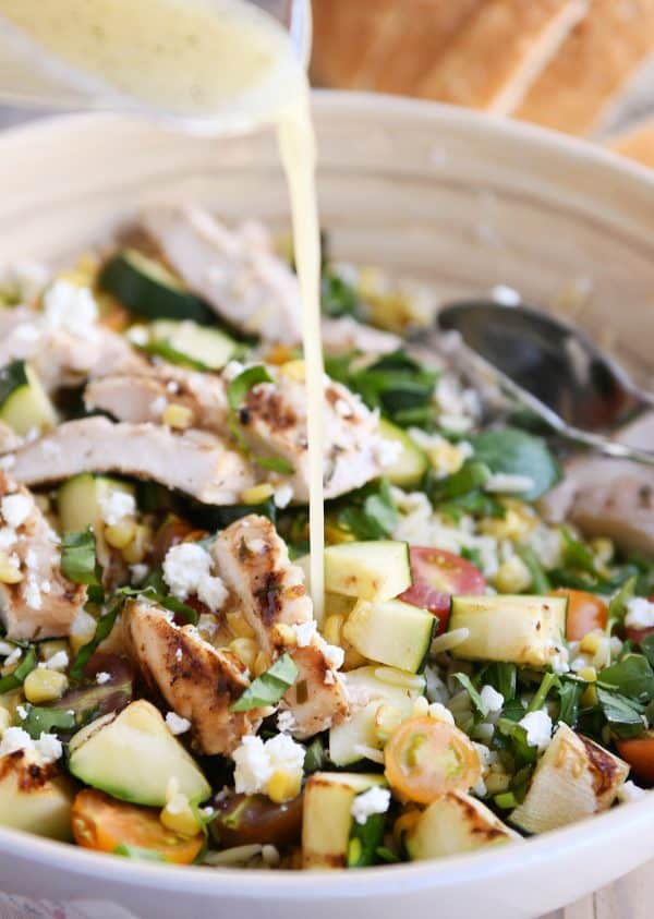 Honey lime dressing being poured onto grilled chicken orzo salad.