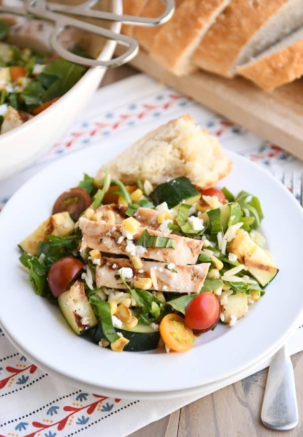 Grilled orzo salad plated on double stacked white plates with rustic crusty bread.