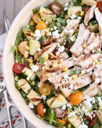 Top down view of grilled chicken orzo salad in white serving bowl.