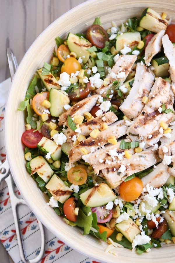 Top down view of grilled chicken orzo salad in white serving bowl.