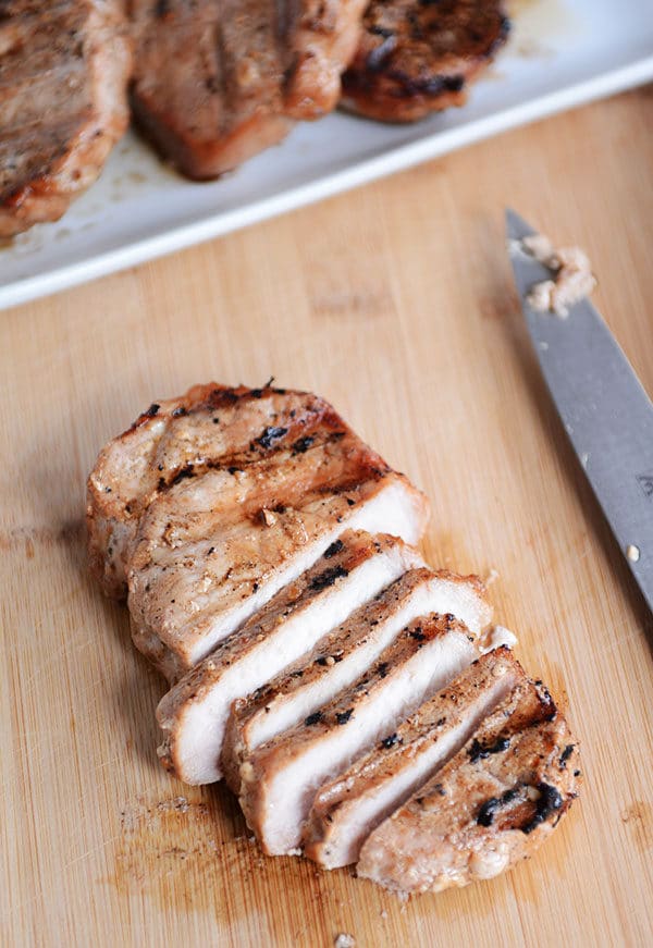 A grilled pork chop sliced up on a cutting board. 