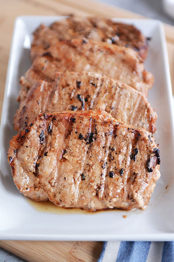 Four cooked, grilled pork chops lined up on a plate. 
