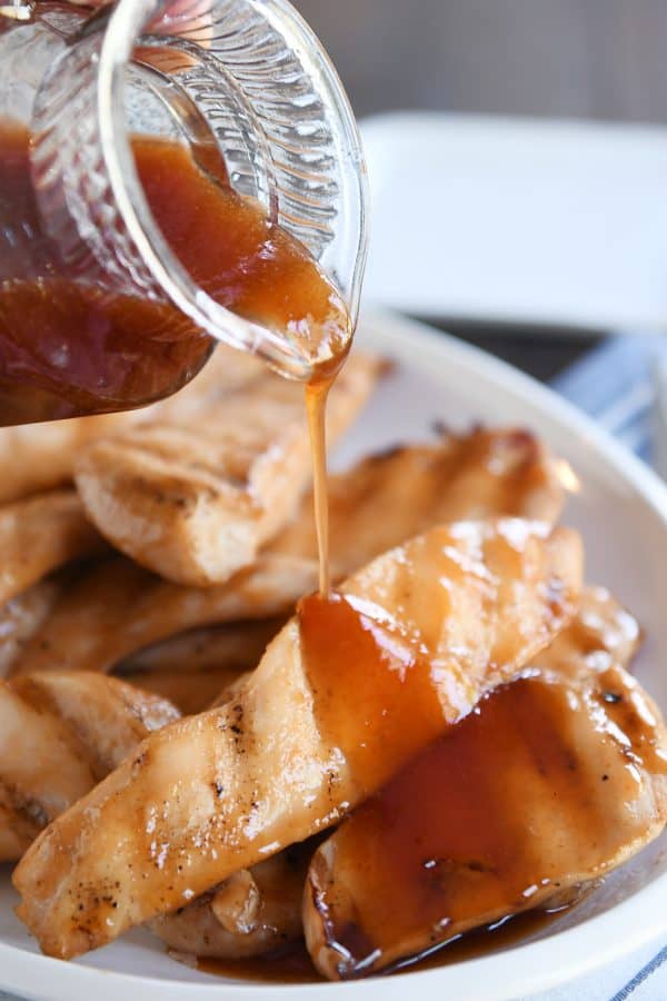 White platter of grilled sweet and sour chicken pieces drizzled with sauce.