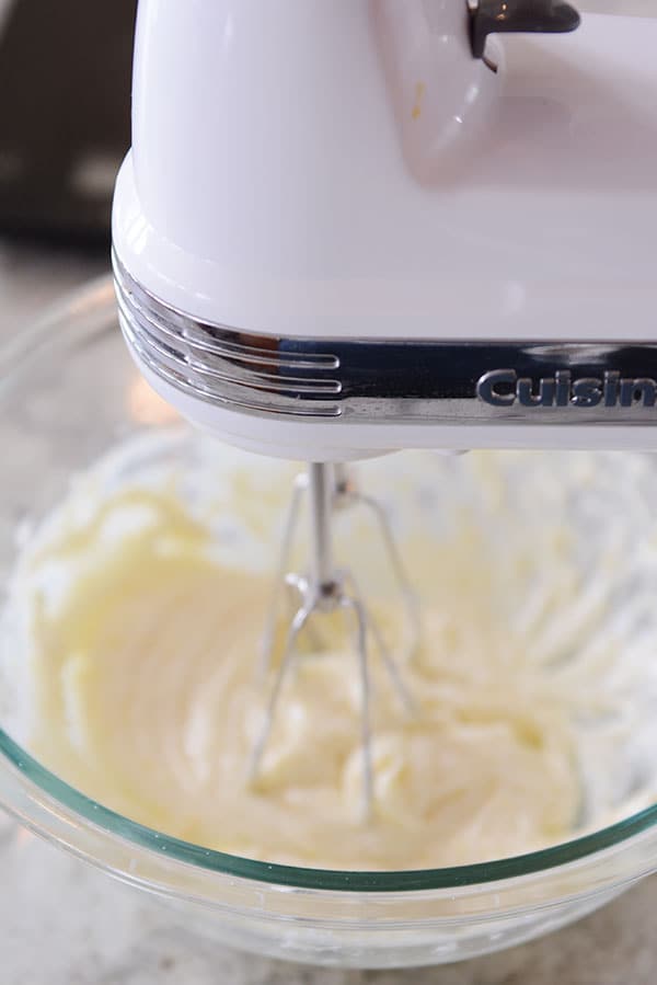 A handheld mixer whipping butter in a clear glass bowl.