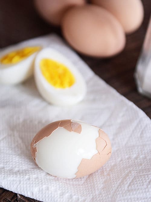 A hard boiled egg cut in half and a partially peeled hard boiled egg in front of it. 
