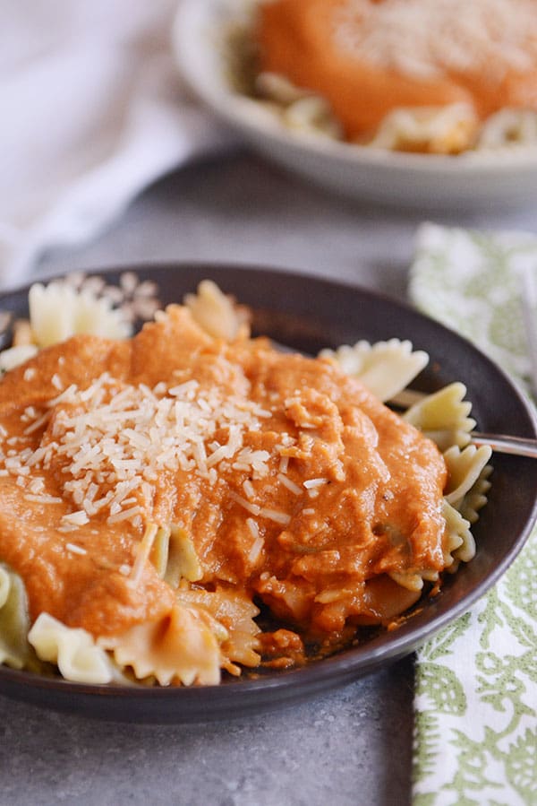 A dark bowl of cooked bowtie pasta with Trader Joe's copycat harvest pasta sauce on top and parmesan cheese.