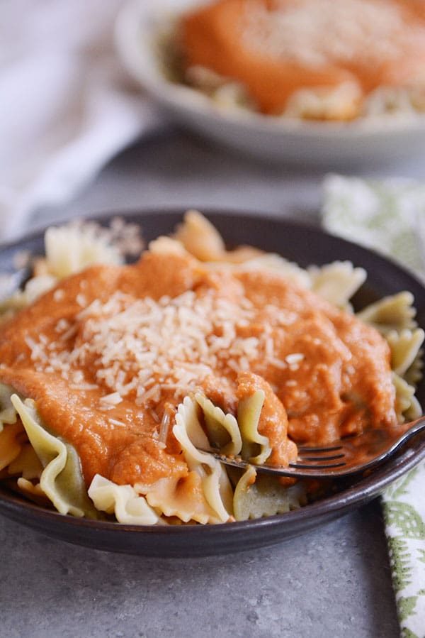 A dark bowl of cooked bowtie pasta with Trader Joe's copycat harvest pasta sauce on top and parmesan cheese.