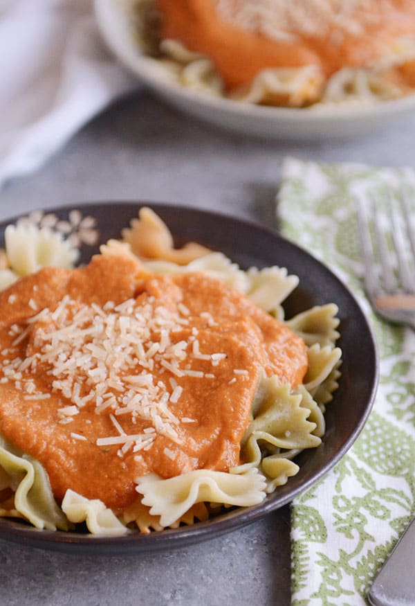 A bowl of cooked bowtie pasta with harvest sauce on top and parmesan cheese.