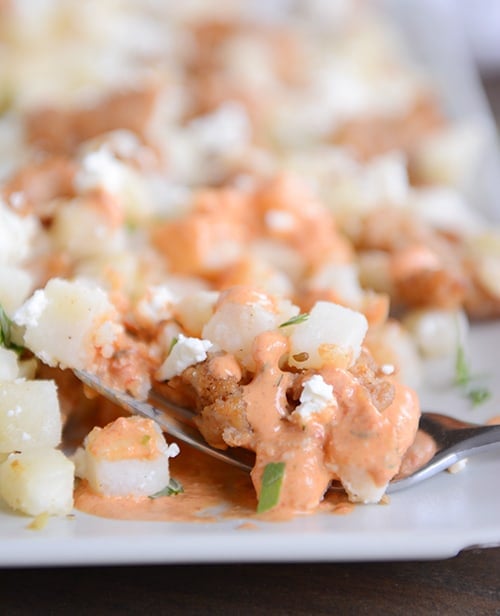 A white tray full of cubed potatoes covered in a red pepper sauce.