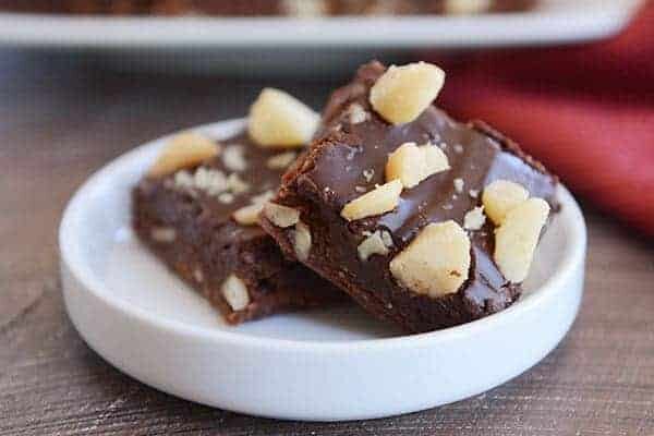 Two chocolate-frosted macadamia nut brownies on a small white ramekin. 