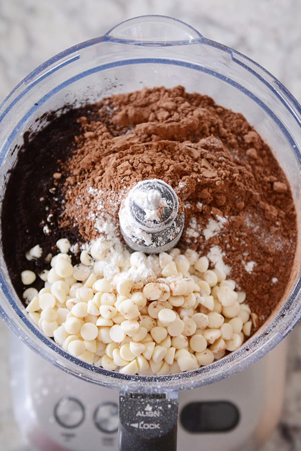 A food processor with white chocolate chips and cocoa ready to be processed.