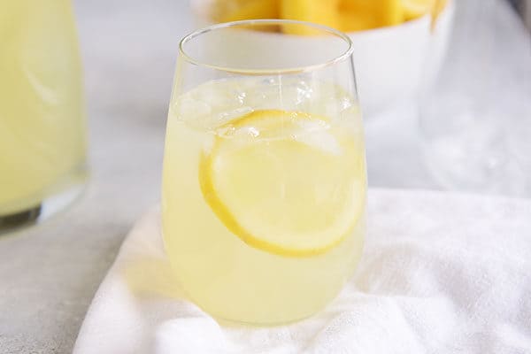 A glass of lemonade with ice and a slice of lemon in it.