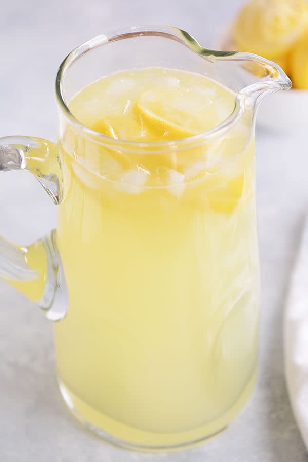 A glass pitcher of fresh lemonade with ice and lemon slices. 