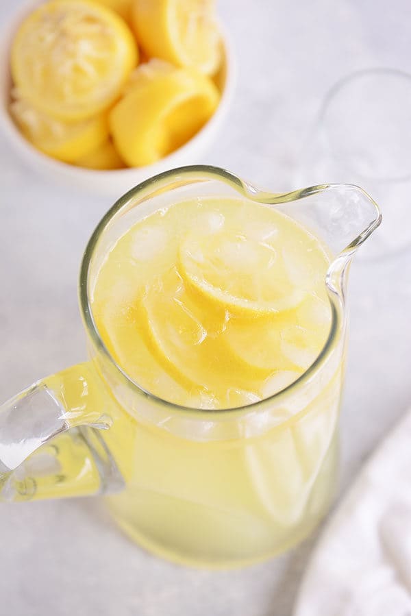 Top view of a glass pitcher of homemade lemonade and a bowl of juiced lemons beside it. 