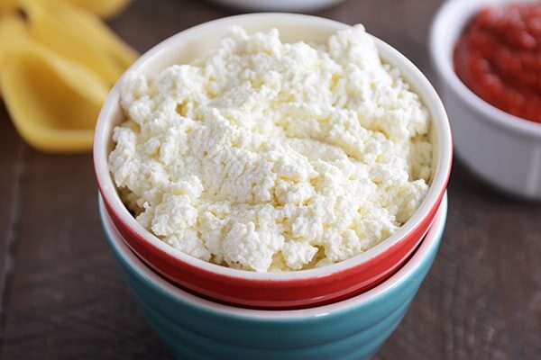 A red bowl full of homemade ricotta cheese.