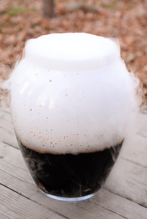 A large glass container full of homemade root beef with dry ice steam coming out the top.