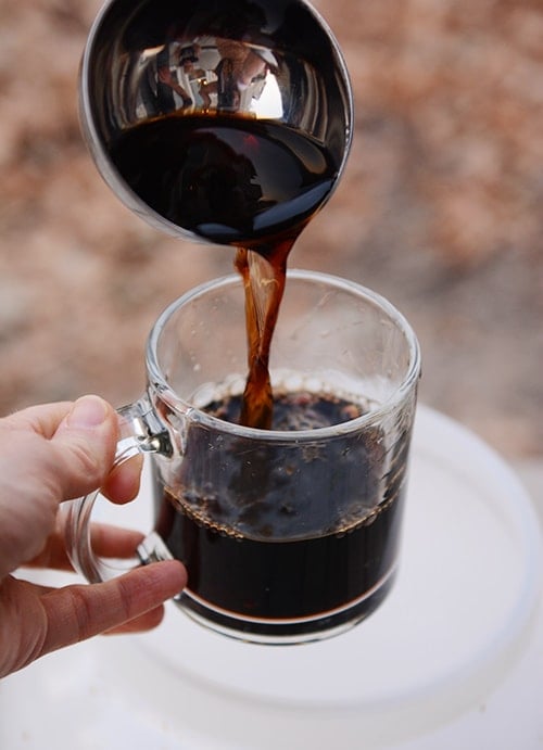 A ladle pouring root beer into a glass cup.