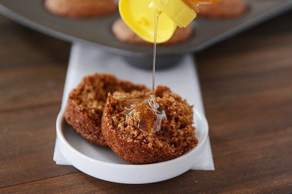 A muffin split in half with honey being poured on top.