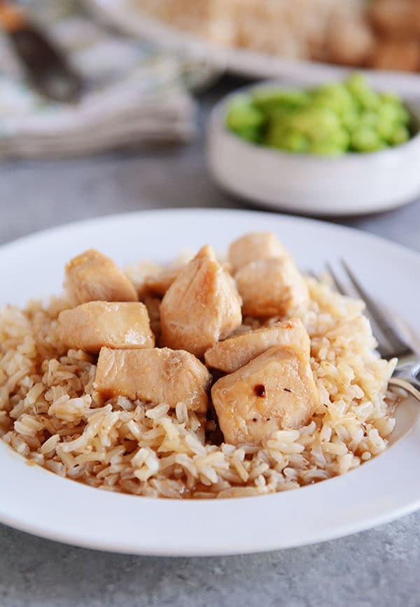 A white plate of cooked brown rice with golden brown chicken cubes on top.