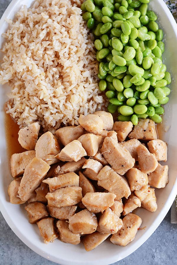 A large white oval platter with cooked chicken, lima beans, and cooked brown rice.