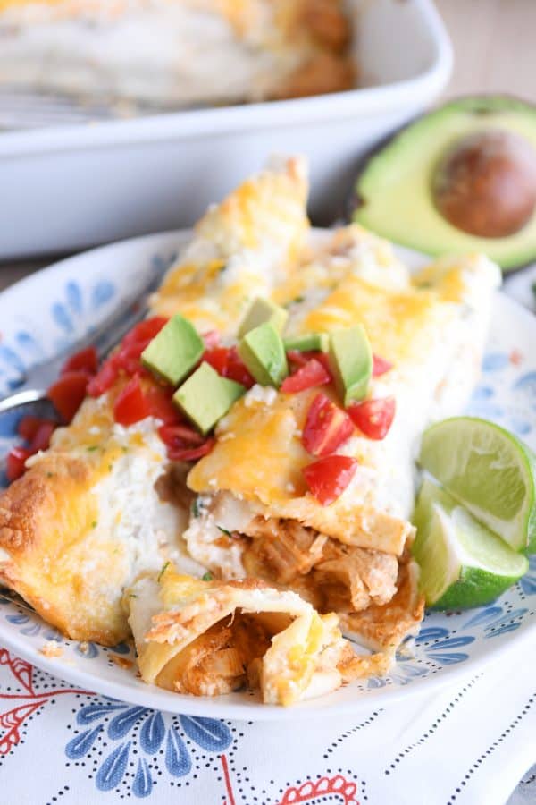 Two honey lime chicken enchiladas on white and blue plate with one bite cut with fork.