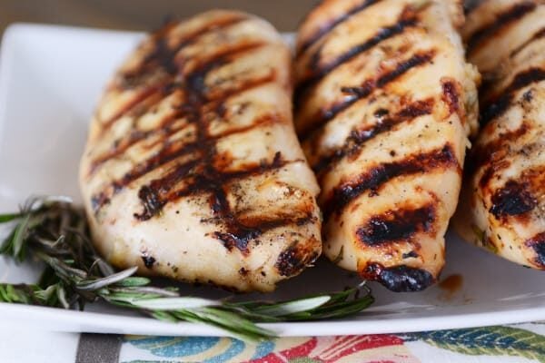 Three grilled chicken breasts lined up on a white platter.