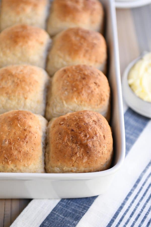 Fluffy honey oat dinner roll sitting on top of pan filled with rolls.