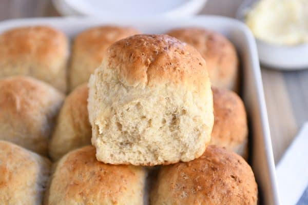 Fluffy honey oat dinner roll sitting on top of pan filled with rolls.