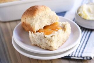 Fluffy honey oat dinner roll on white plate with butter and apricot jam.