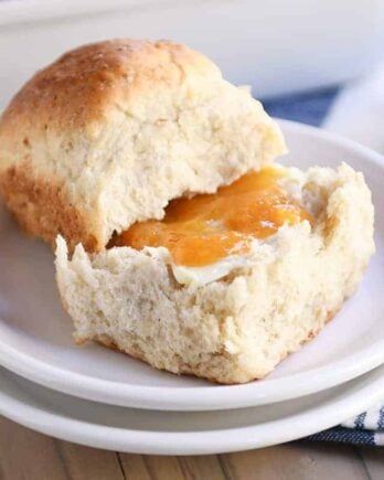 Fluffy honey oat dinner roll on white plate with butter and apricot jam.
