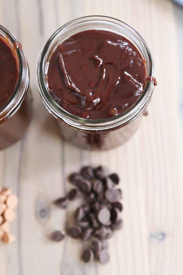 Rich chocolate 5-minute hot fudge sauce in jar with chocolate chips on counter.