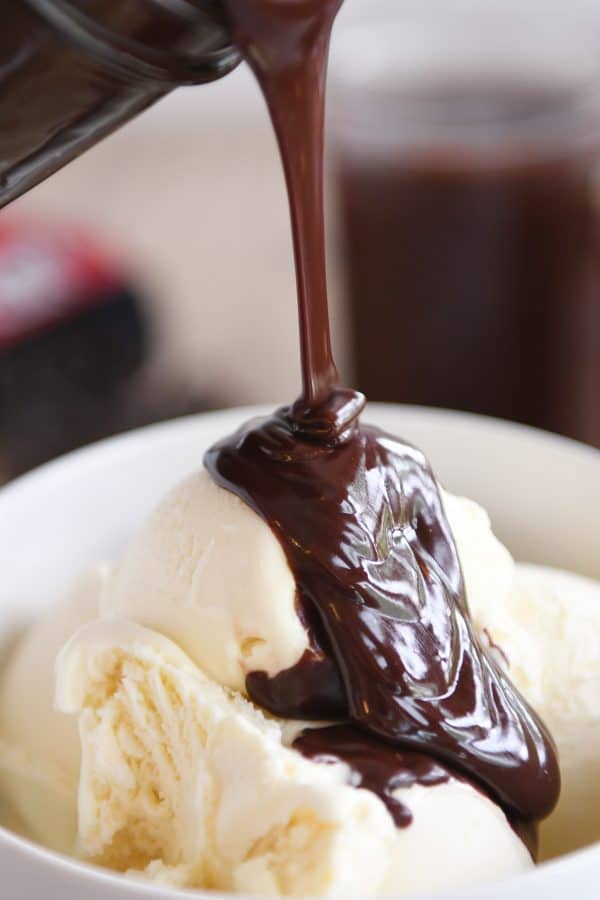 Vanilla ice cream in white bowl with 5-minute hot fudge sauce being poured on top.