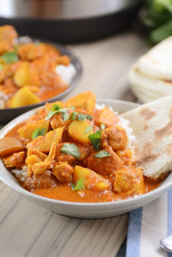 A bowl of white rice topped with Indian butter chicken and potato curry. 