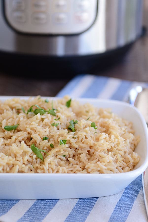 A white dish full of cooked brown rice pilaf, with an Instant Pot in the background.
