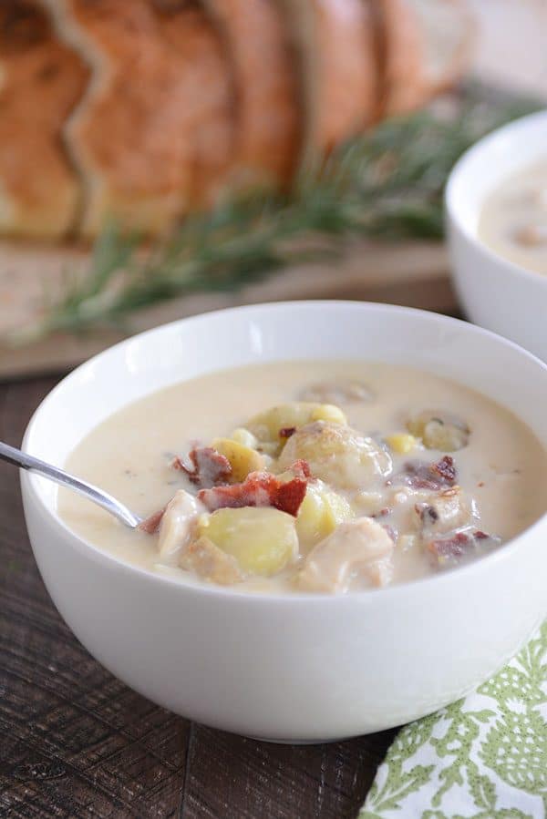 Two bowls of potato soup, topped with crumbled bacon, with fresh sage and a loaf of bread in the background.