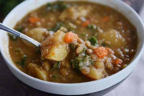 A white bowl of soup filled with cooked lentils, carrots, sausage, potato, and spinach. 
