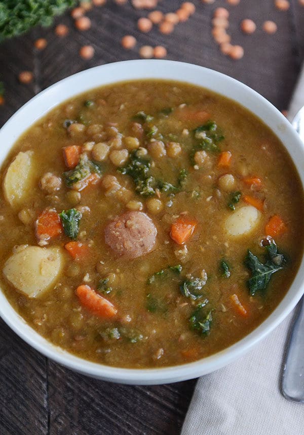 A bowl of soup filled with cooked lentils, carrots, sausage, potato, and spinach. 