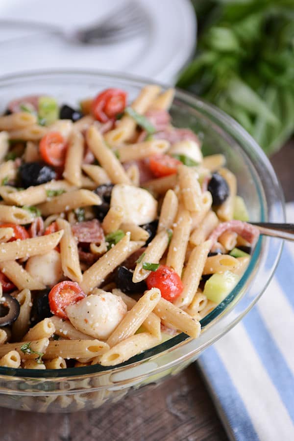 A glass bowl full of Italian pasta salad with olives, tomatoes, and mozzarella.