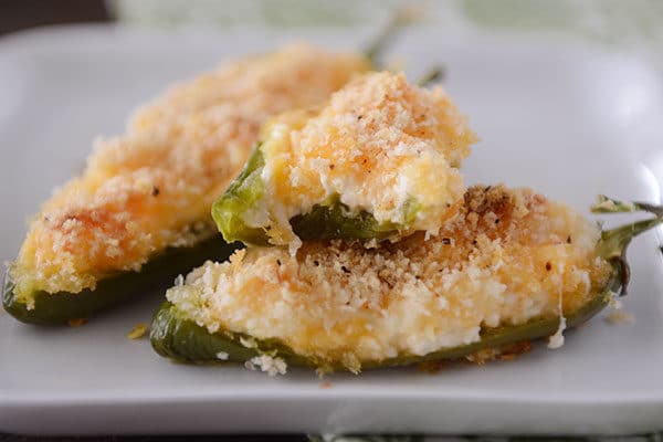 Three cooked jalapeno poppers, one with a bite taken out, on a white plate.