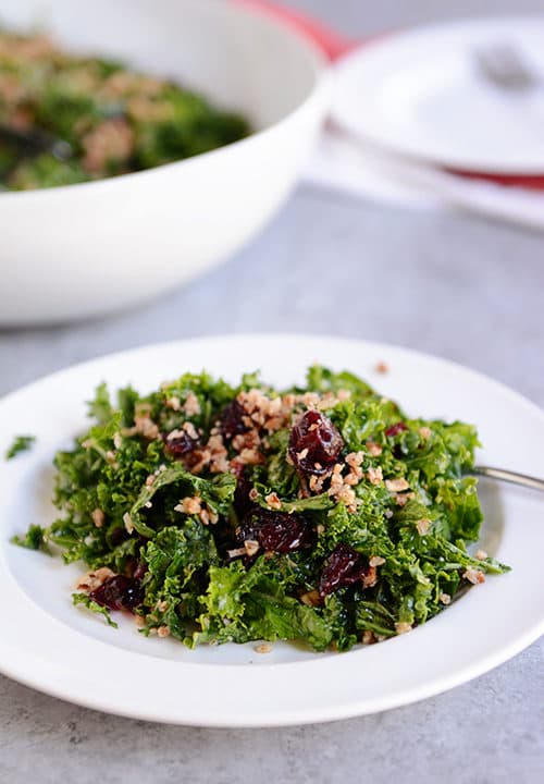 A large helping of cranberry pecan kale salad on a white plate.