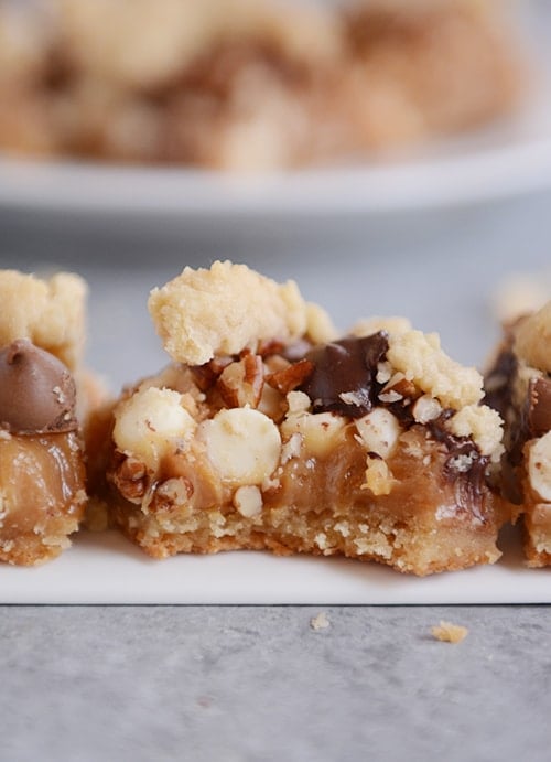 caramel pecan chocolate chip toffee bars lined up with the middle bar with a bite taken out