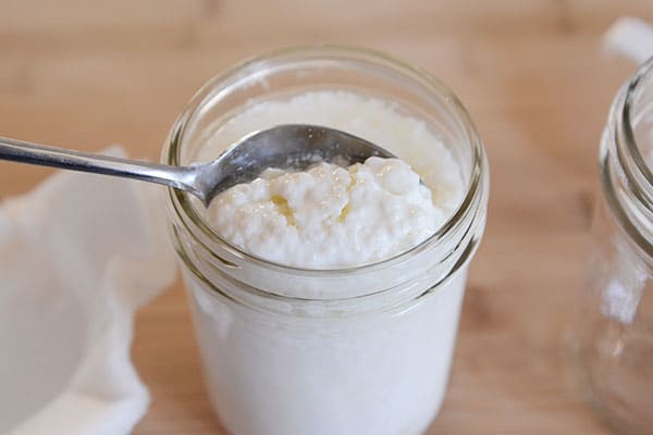 Spoon scooping out kefir grains from a mason jar.