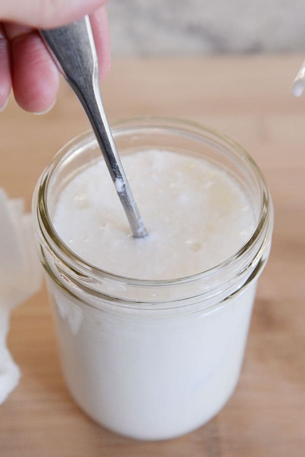 A spoon getting stirred into a mason jar of kefir grains and milk. 