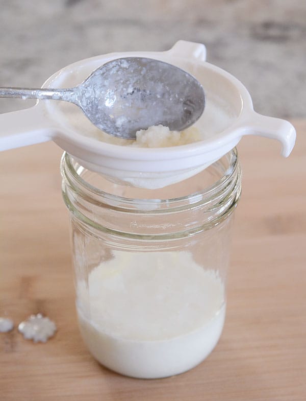 Kefir grains in a strainer over the top of a mason jar. 