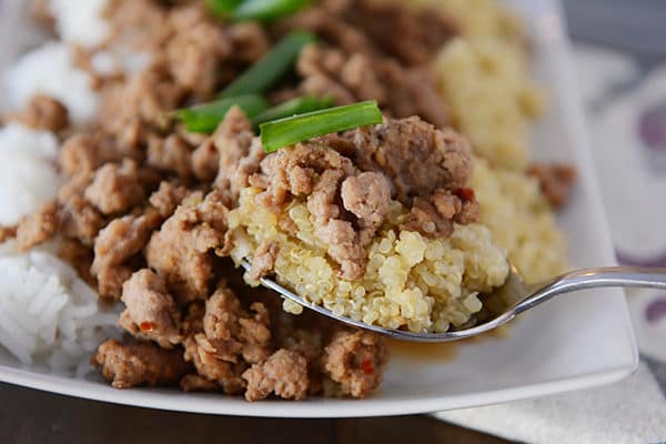 A scoop of cooked quinoa and beef over a tray with more beef and cooked rice.
