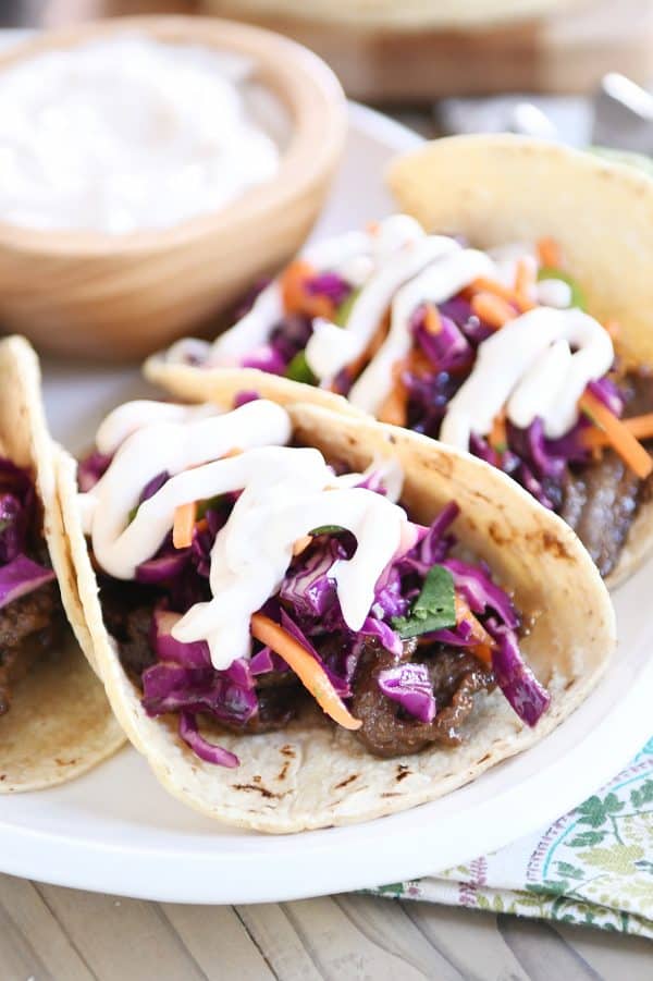 Korean beef tacos with slaw and sauce on white platter.