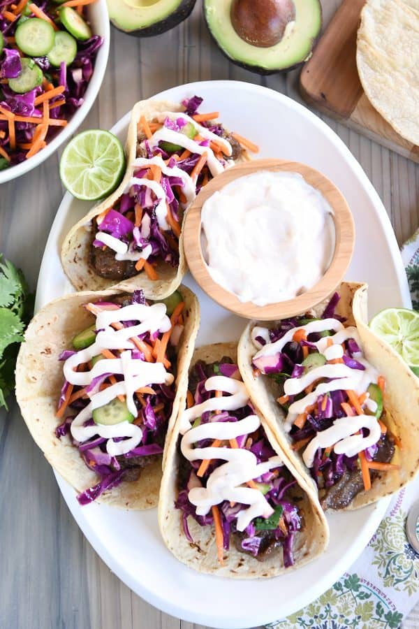 Top down view of four Korean beef tacos with slaw and sauce on white platter.